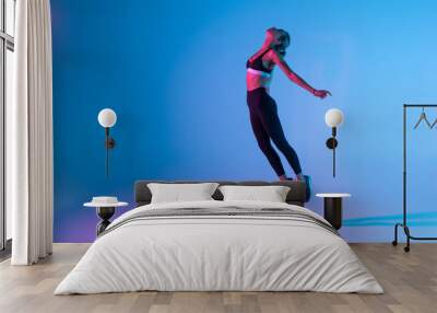 Sporty young woman fitness jumping isolated on purple light background Wall mural